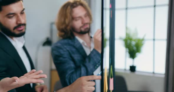 Coworkers Brainstorming New Ideas Near Glass Board with Colourful Sticky Notes with Reminders