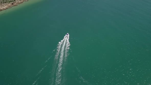 Motorboat crossing lagoon navigates deep channel near shore, aerial