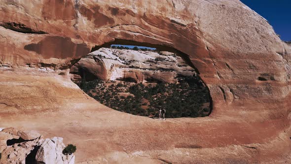 Drone Flying Through Massive Arches Rock Formation with Two Tourists in the Middle at National Park