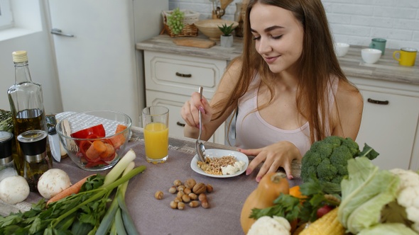 Lovely Girl Eating Raw Sprouts Buckwheat with Nuts in Kitchen with Fresh Vegetables and Fruits