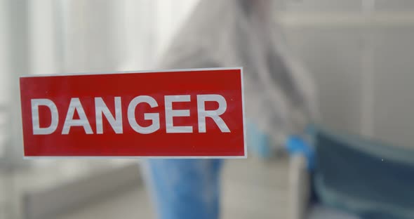 Danger Sign Hanging on Door of Isolation Ward with Doctors Moving Bed with Patient on Background