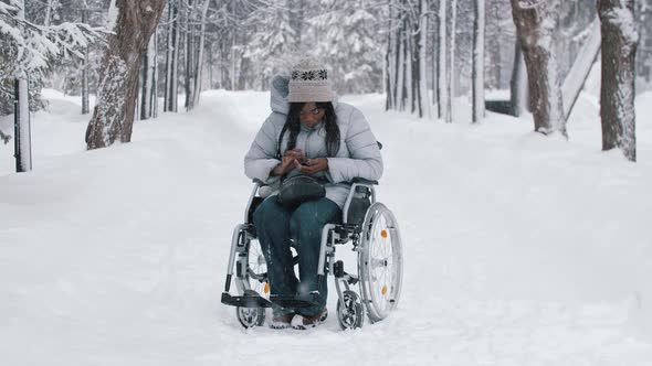 Young Black Woman Sitting in a Wheelchair and Using Her Phone