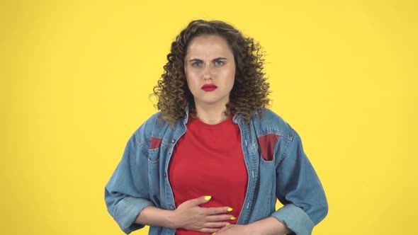 Cute Female Feels Very Bad, Her Stomach Hurts on Yellow Background at Studio, Slow Motion