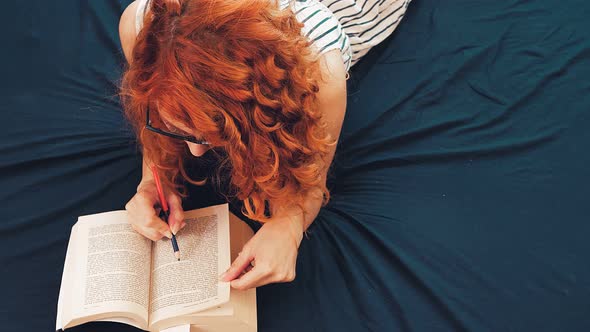 study hard - young woman lying on the bed points out the book