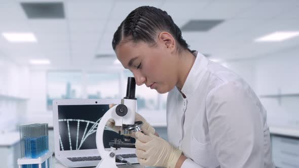 A Female Lab Technician Sitting at a Table Next To a Laptop in a Modern Medical Laboratory