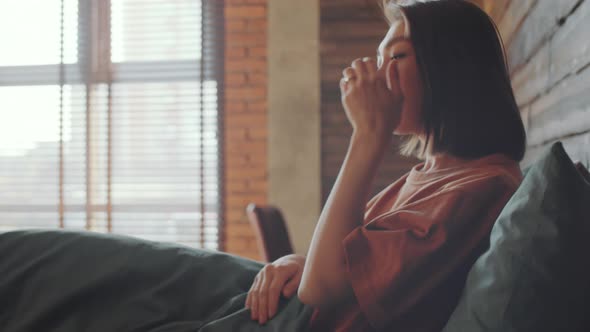 Asian Woman Using Smartphone after Waking Up in Bedroom