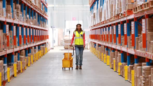 Female warehouse worker walking with mop and bucket