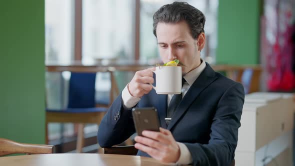Portrait of Absorbed Elegant Man Drinking Tea in Restaurant and Surfing Internet on Smartphone