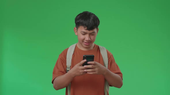 The Front View Of Asian Boy Student Using Mobile Phone While Walking To School On Green Screen