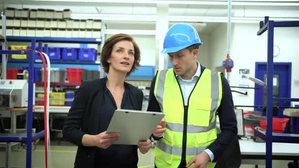 Female manager with clipboard speaking with coworker in factory