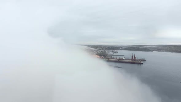 Aerial view through a cloud to a pier in a coastal town (Quebec, Canada)