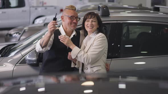 Excited Caucasian Wife Hugging Husband Bragging Car Key in Dealership in Slow Motion