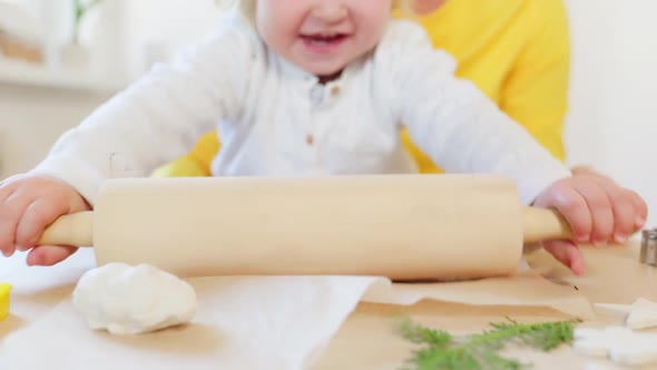 A happy little girl rolls out cookie dough with a rolling pin. Homemade Christmas cookies.