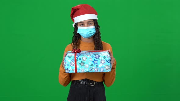 Sad Teen African American Girl in Coronavirus Face Mask Holding Christmas Gift Looking at Camera on