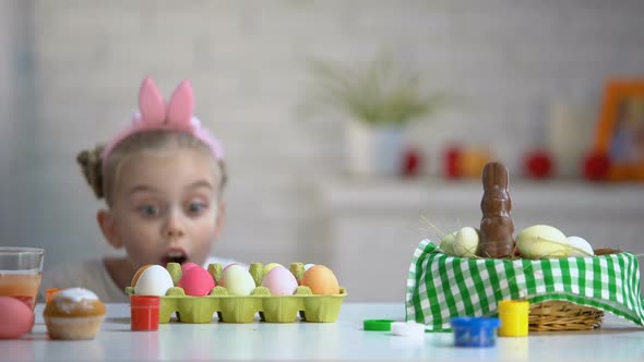 Funny Girl Appearing From Under Table and Excitedly Looking at Dyed Easter Eggs