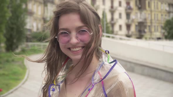 Close-up Portrait of Pretty Young Woman in Sunglasses Standing Outdoors on Rainy Day and Smiling at