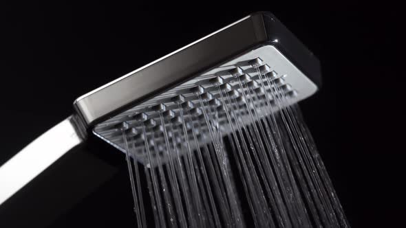 Water running from shower head in bathroom with black background, close up