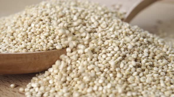 Pouring raw quinoa seeds into a wooden spoon in slow motion