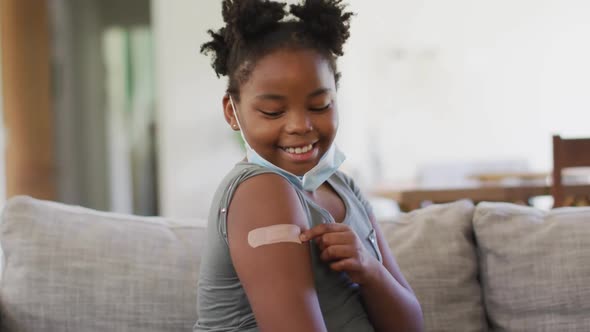 African american girl wearing face mask pointing at bandage on her arm