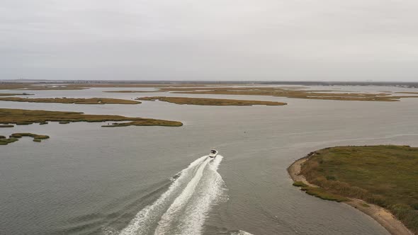 drone camera trails behind a boat, as it leaves behind a beautiful white wake in the green waters of