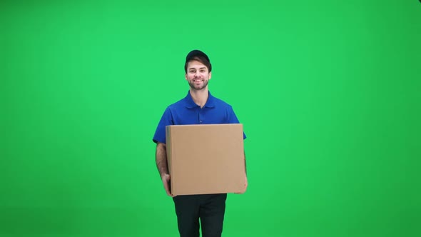 Cheerful Man Courier in Uniform Walks with a Cardboard Box in His Hands on a Green Background