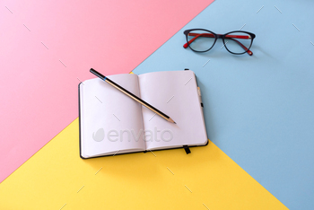 Open notebook with blank pages, pencil and glasses on colorful geometric background