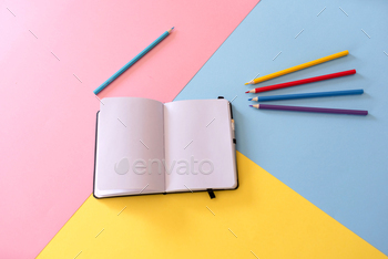 Open notebook with blank pages and colored pencils on colorful geometric background