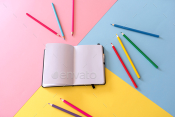 Open notebook with blank pages and colored pencils around on colorful background