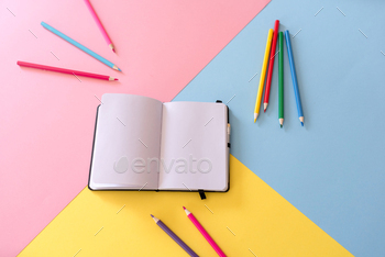 Open notebook with blank pages and colored pencils around on colorful geometric background