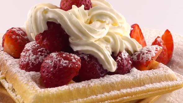 Belgian waffles with strawberry, whipped cream and powdered sugar on a plate