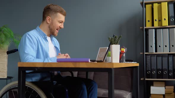 Motivated Cheerful Disabled Freelancer Talking on Video Chat While Sitting at Office in a Wheelchair