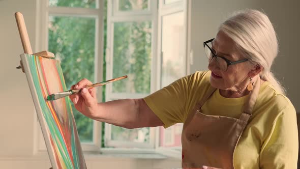 Senior Woman Artist Paints a Picture on Canvas