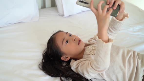 Calm Asian Child Playing Game on Cellphone Lying on Bed