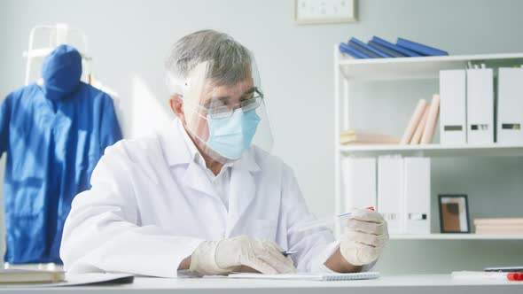 PCR Test in Laboratory Aged Doctor in Glasses Holding COVID19 Swab Collection Kit and Writing the