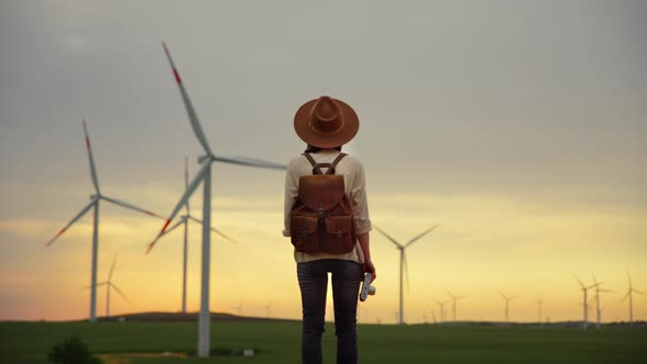 Young photographer with retro camera looking at windmills in field