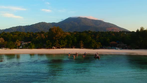 An aerial shot from the ocean side facing white sand beach, resort, green trees and mountain.