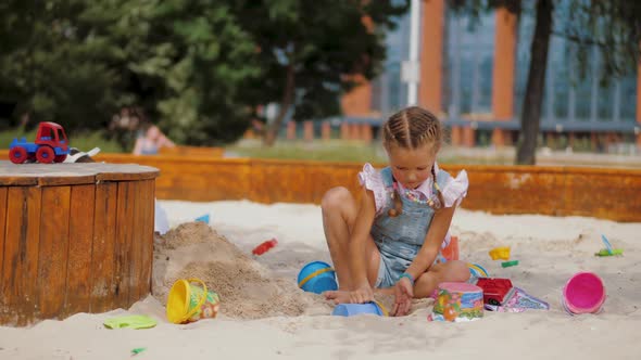 Little Girl Playing with Plastic Toys and Buckets in Sandbox at Residential Area