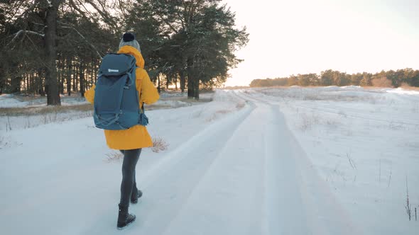 A Young Caucasian Girl with Backpack Going on Winter Forest Road in Snow Covered Winter Pine Forest