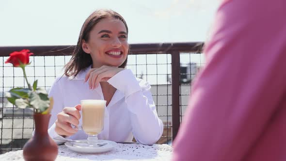 Woman Drinking Coffee At Cafe With Friend Outdoors