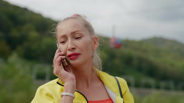 Adult Woman with Ponytail is Talking By Mobile Phone Outdoors Walking in Mountain