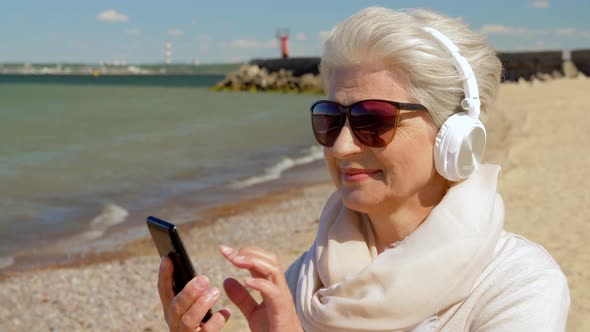 Old Woman in Headphones with Smartphone on Beach