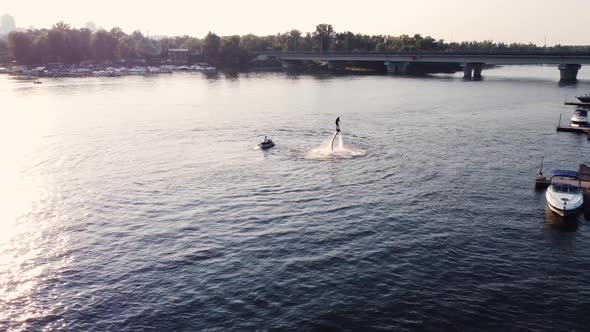 young guy is riding a flyboard near the pier. training. sunset. Drone view.