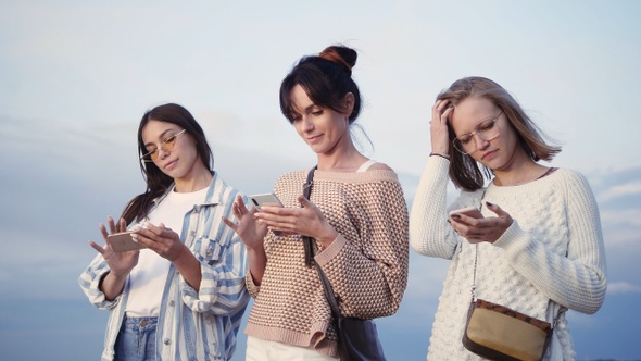 Three ladies texting in their smart phones in the street.