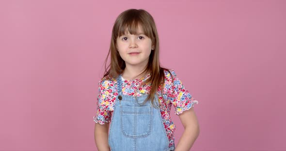 Sweet Little Girl 6-7 Years Old Posing in Dungarees Jeans and Flower Pattern Blouse on Pink