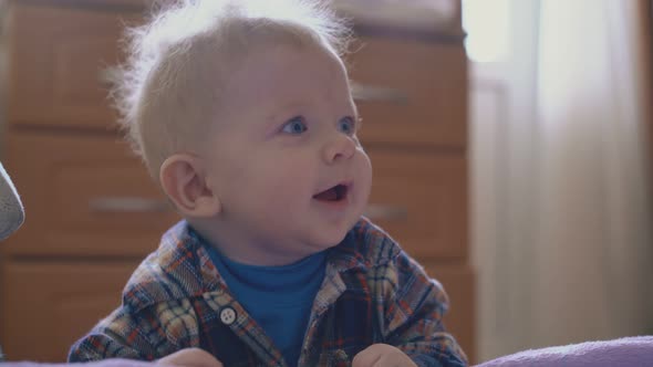 Happy Boy with Blond Hair Plays with Thin Tube at Large Bed