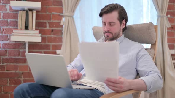 Casual Young Man with Laptop Working on Documents on Sofa