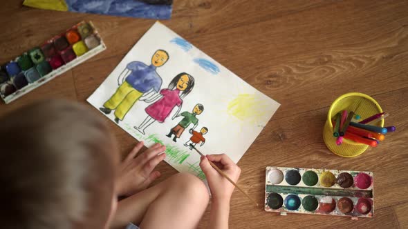 A Child Paints a Drawing on the Floor with Watercolors