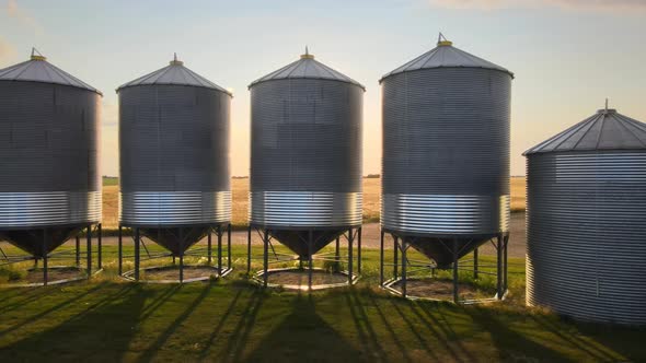 Sidewaysing drone footage of big metal grain bins in rural Alberta with the low standing sun lurking