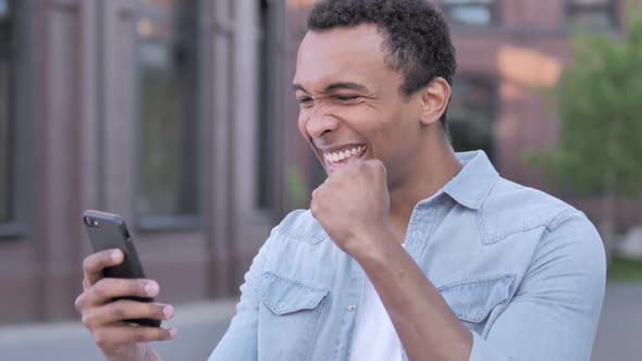 Outdoor African Man Excited for Success on Phone