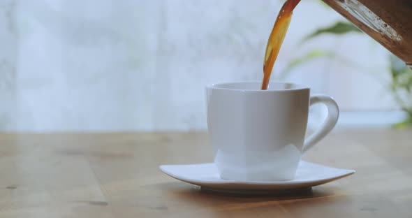 Man's Hand Pours Coffee Into a Cup on a Wooden Table By the Window